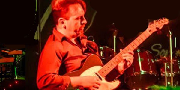Man passionately playing electric guitar on stage under red lighting.