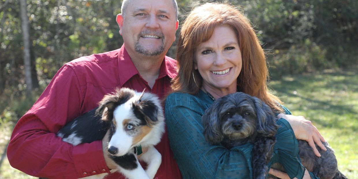 Smiling couple outdoors holding two dogs on a sunny day.