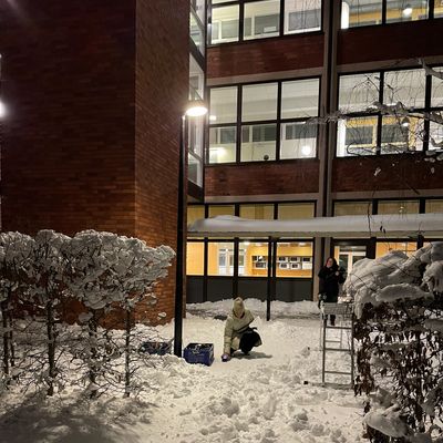 Two people in a snowy courtyard at night near an apartment building.