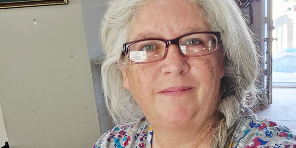 Smiling woman with gray hair and glasses indoors.
