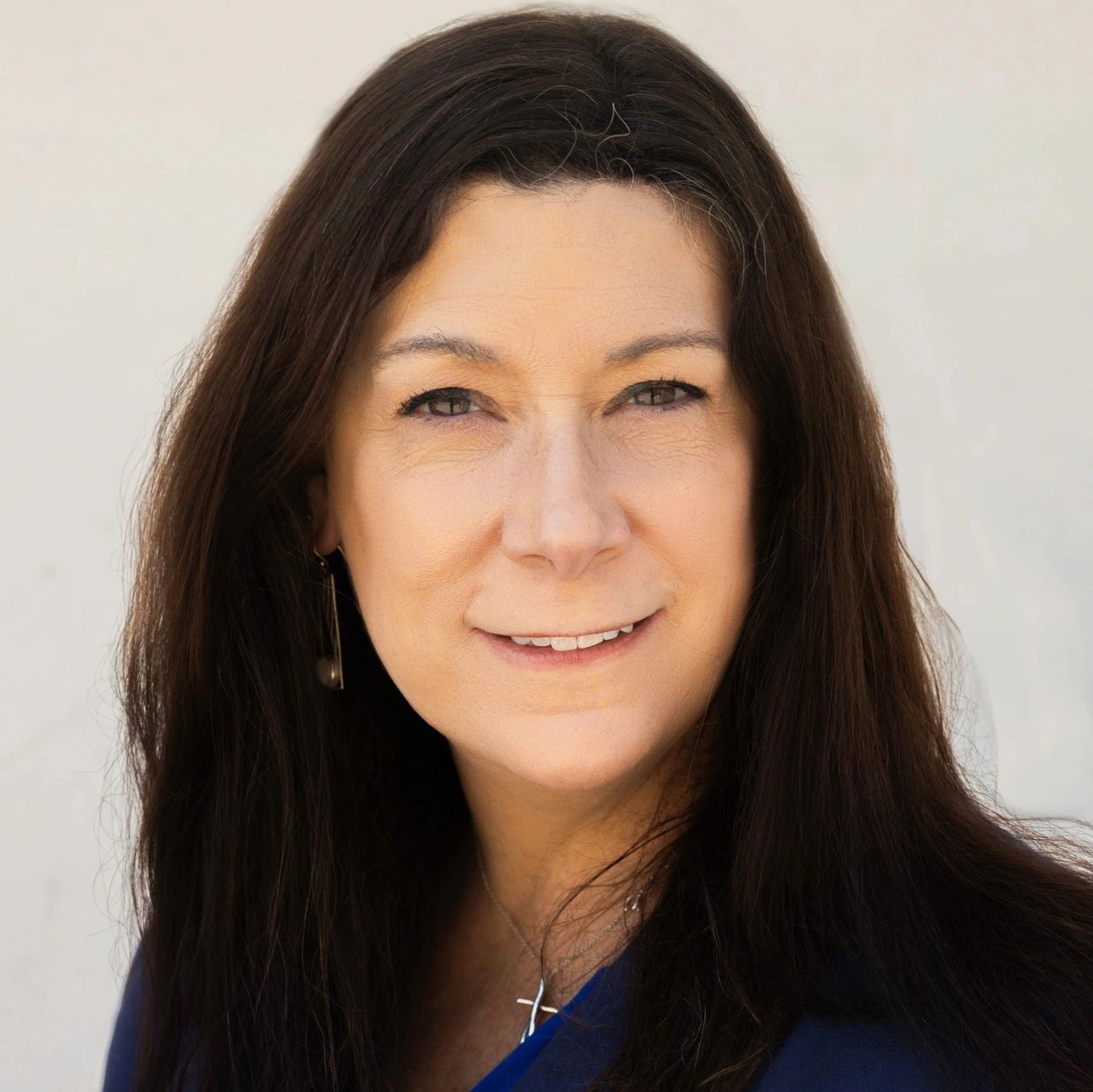 Confident woman with long dark hair wearing a blue blazer and cross necklace.
