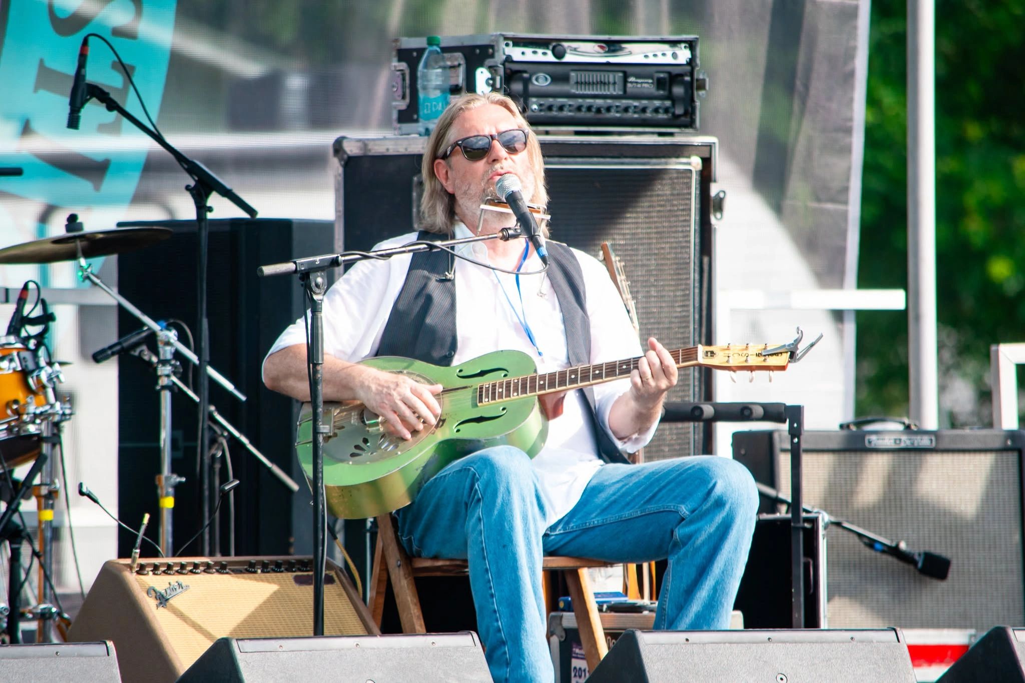 Musician playing guitar and singing on stage at an outdoor event.