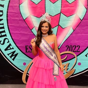 Beauty queen in a pink gown with a crown and sash.