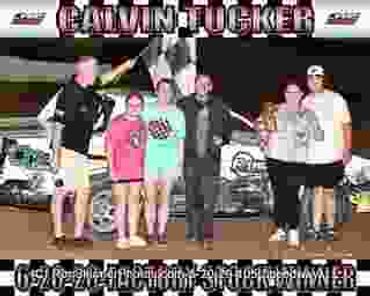 A group celebrating a racing victory in front of a car with trophies.