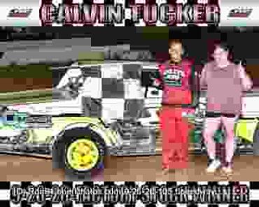 Two men celebrating beside a race car with a winner banner.