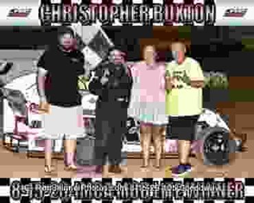 Four people celebrate a racing win at night by a car.