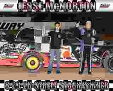 Two men celebrating in front of a race car and banner.