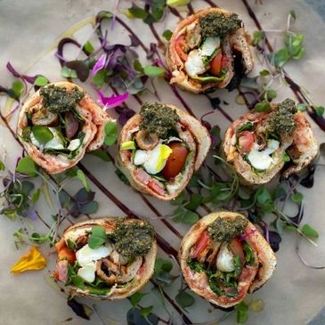 Colorful vegetable wraps garnished with herbs and drizzled sauce on a marble surface.