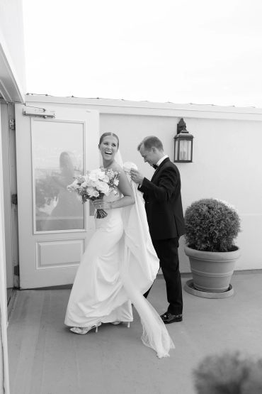 Bride laughing joyfully as groom adjusts her dress.