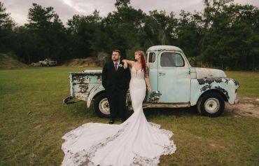 Bride and groom posing by an old truck in a field.