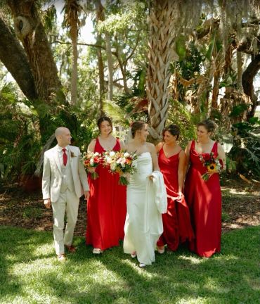 Bride and bridesmaids in red dresses outdoors.