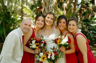 Smiling wedding party with bride and bridesmaids in red dresses.