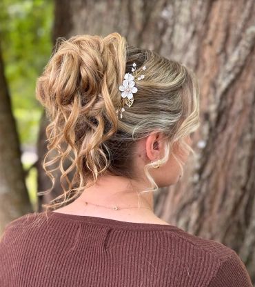 Elegant curly updo hairstyle with floral hair accessory.
