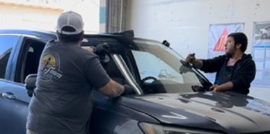 2 technicians setting a new windshield onto a vehicle.