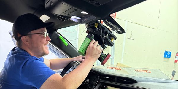 Technician working on cutting a broken windshield out of a vehicle.