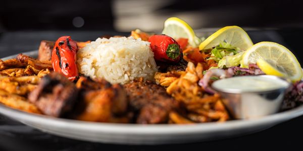 A plate of grilled meat, rice, roasted peppers, fries, and salad with lemon wedges.