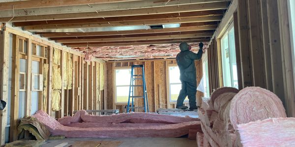 Worker installing pink insulation in a house under construction.