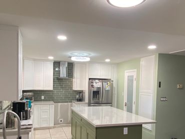 Modern kitchen with green island and white cabinets under renovation.