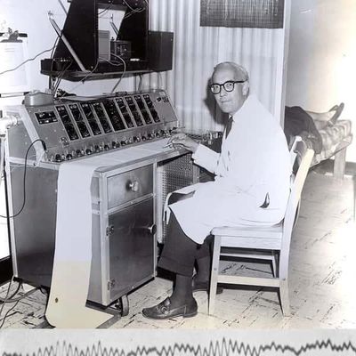 Scientist operating an old scientific instrument in a lab, black and white photo.
