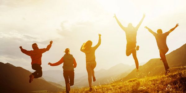 A group five young people cavort on an open hillside while the sun rises before them.