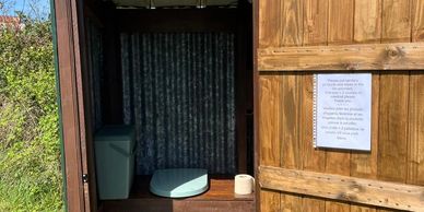 Rustic outdoor toilet with wooden door and basic amenities inside.