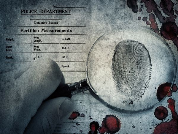 A magnifying glass reveals a fingerprint on a police Bertillon measurements sheet with blood stains.
