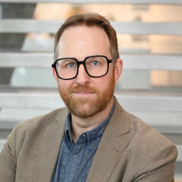 Man with glasses and beard wearing a blazer.
