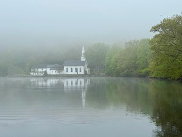 A white church and trees reflected on a misty lake.