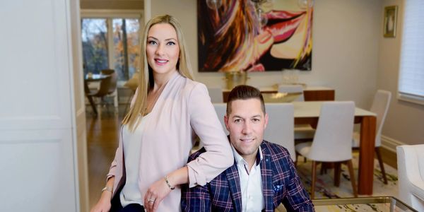 A stylish couple posing in a modern, well-lit living room with contemporary art.