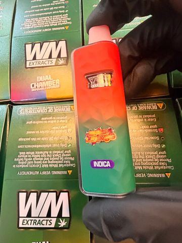 Hand holding a colorful WM Extracts vape device labeled Indica.