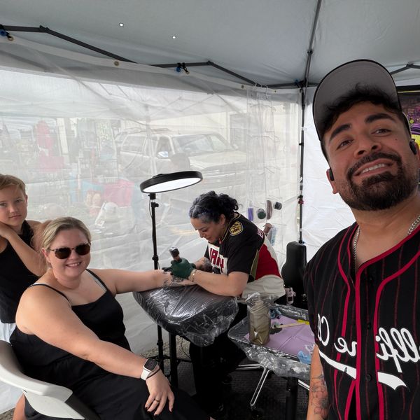 Tattoo artist working on a woman's arm inside a tent.