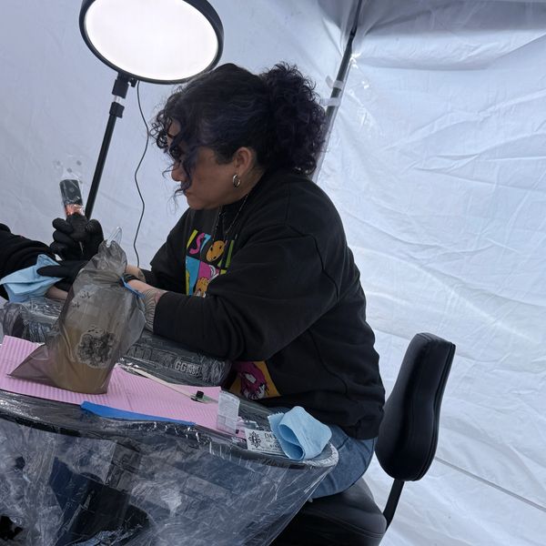 Tattoo artist working on a client in a tent.