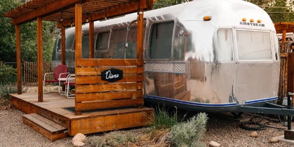 Shiny Airstream trailer with wooden porch named Diana in a rustic outdoor setting.