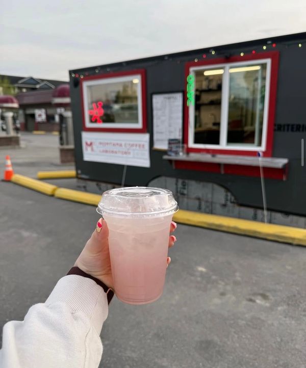 Hand holding a pink iced drink in front of a black food stand.