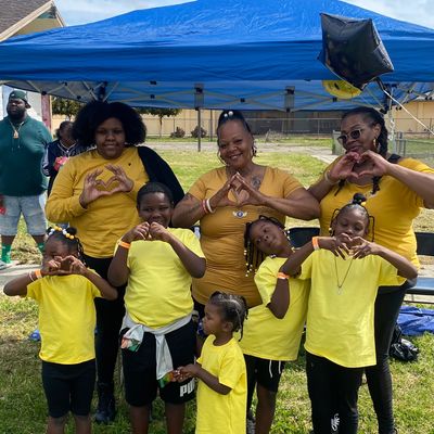Group of smiling people in yellow shirts making heart shapes with their hands outdoors.