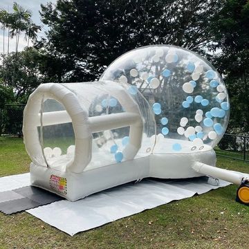 A large inflatable bubble with blue and white balloons inside on a lawn.