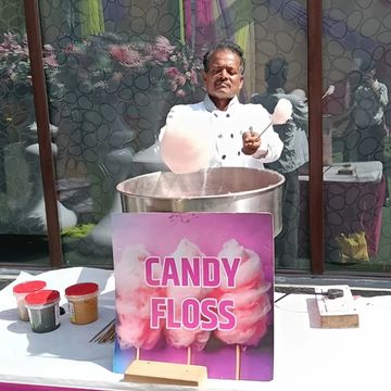 Man making candy floss at an outdoor stall with a colorful sign.