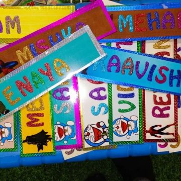 Colorful name tags with glitter letters and cartoon characters arranged on a blue surface.