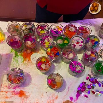 Colorful decorative candles with beads and shells on a paint-stained table.