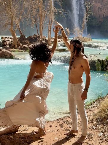 Couple dancing near a turquoise waterfall under bare trees.