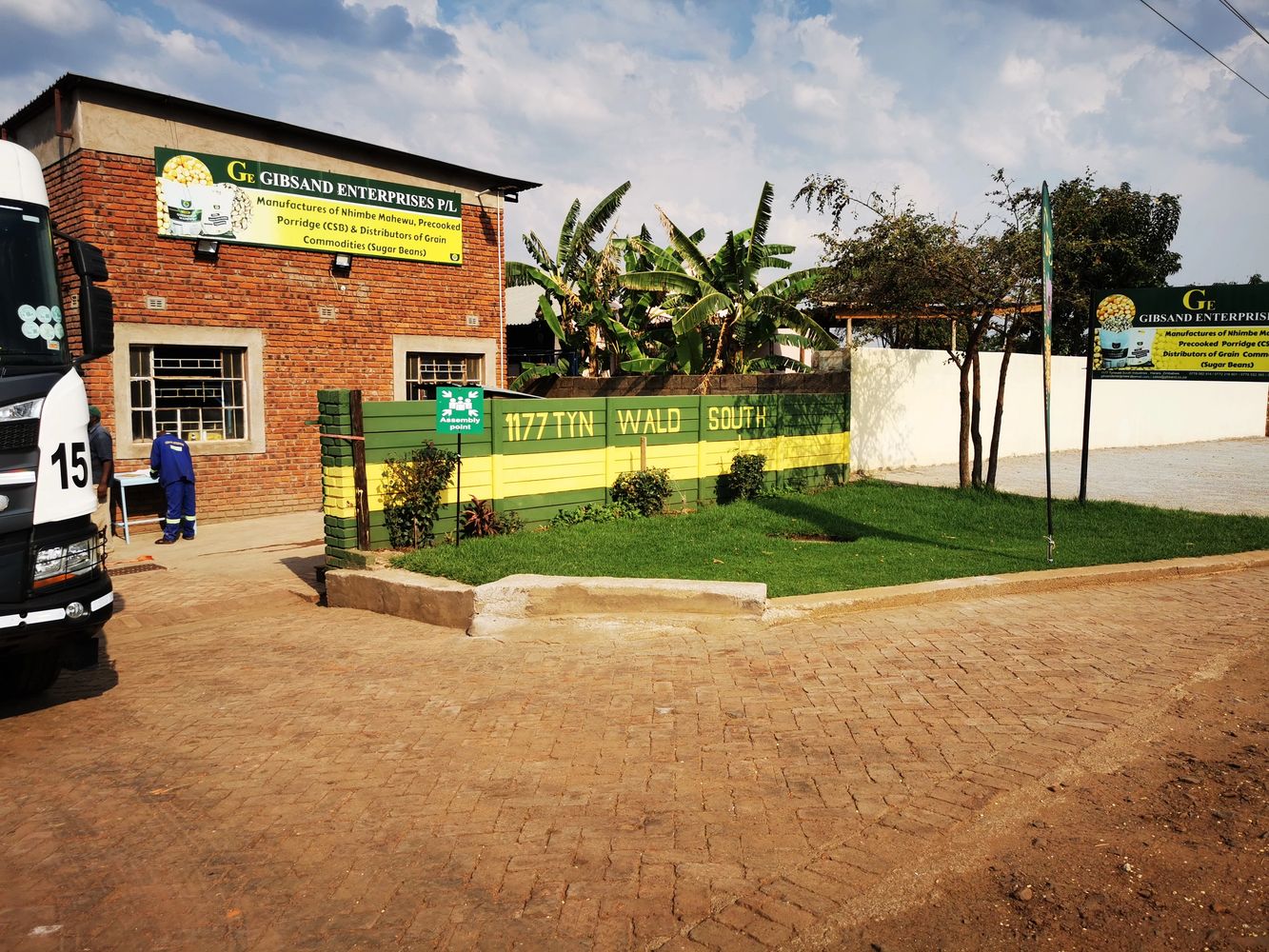 Brick building of Gibsand Enterprises with green and yellow fence and truck nearby.