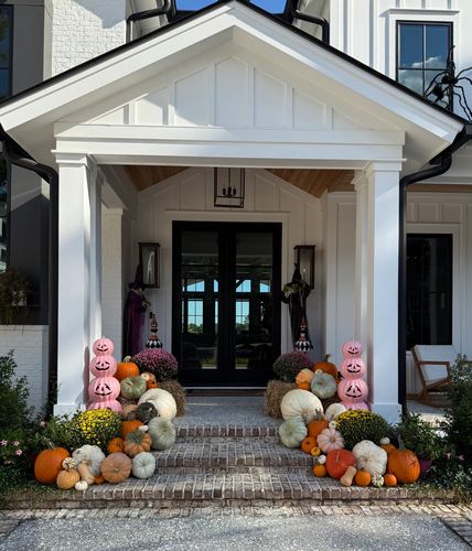 Elegant porch decorated with pumpkins, flowers, and Halloween-themed pink jack-o'-lanterns.