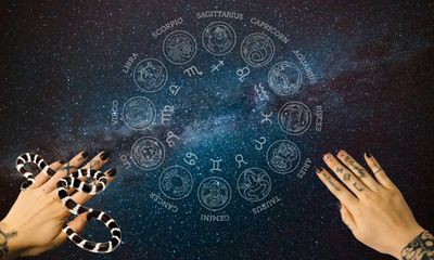 Two tattooed hands reach up, the left one with a snake on it. The center is a blue zodiac wheel