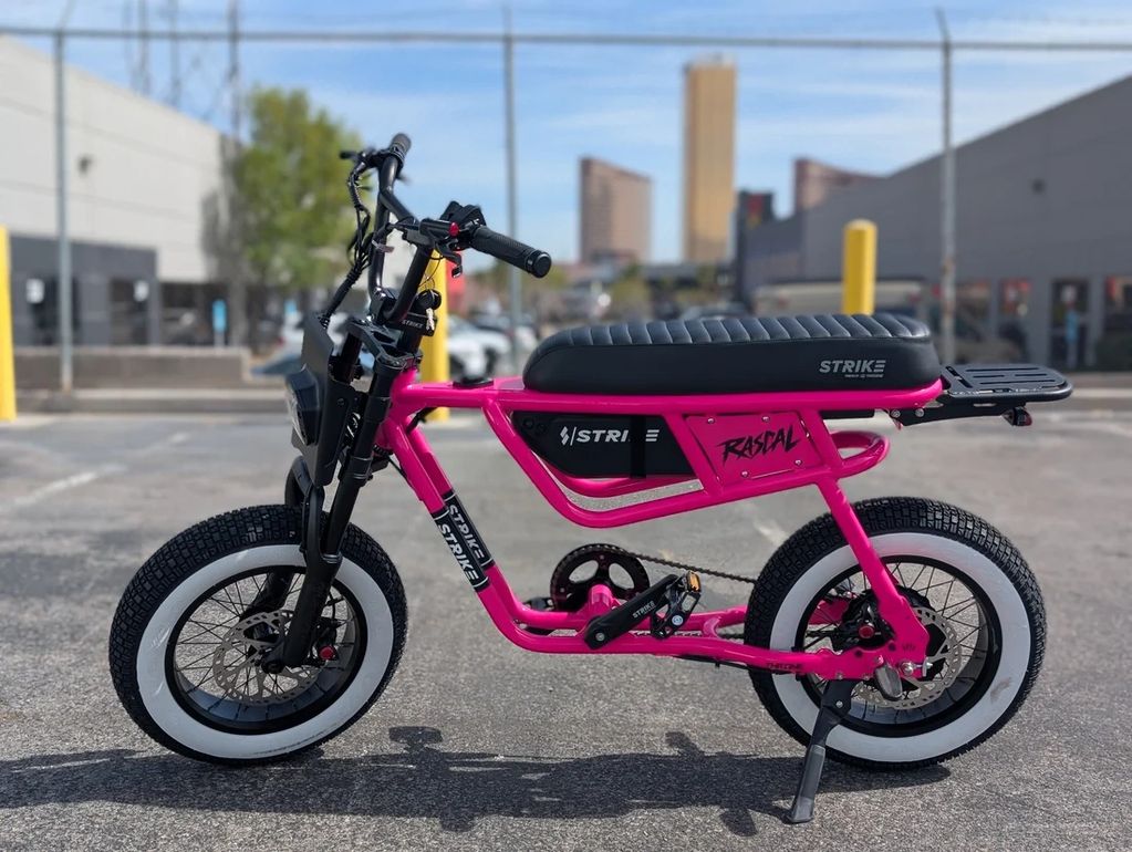 Bright pink electric bike with white-wall tires parked outdoors.
