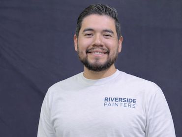 Smiling man wearing a Riverside Painters shirt against a dark background.
