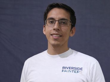 Man wearing glasses and a Riverside Painters white shirt smiling.