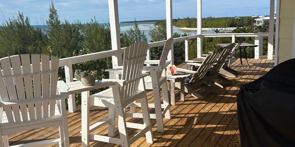 A sunny porch with white chairs overlooking a scenic coastal view.