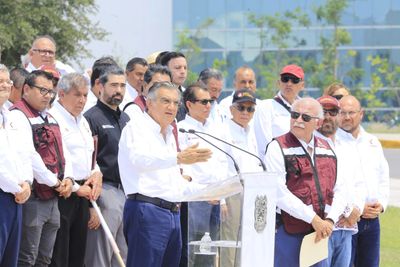 A man speaks at a podium surrounded by a group of people outdoors.
