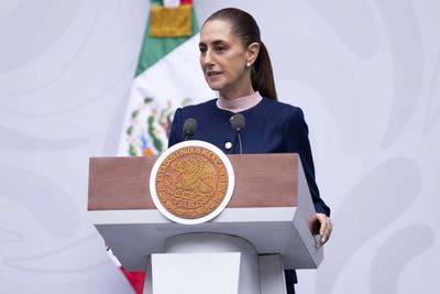 Mujer dando un discurso oficial frente a un podio con el escudo de México.