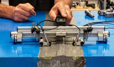 Hands operating a precision measuring device on a metal surface in a workshop.
